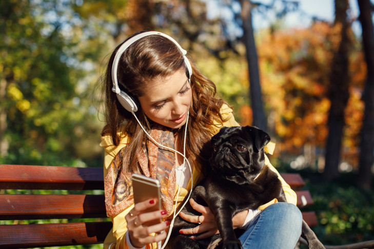 パグと、音楽を聴いているスマートフォンで屋外に座っている若い女性。