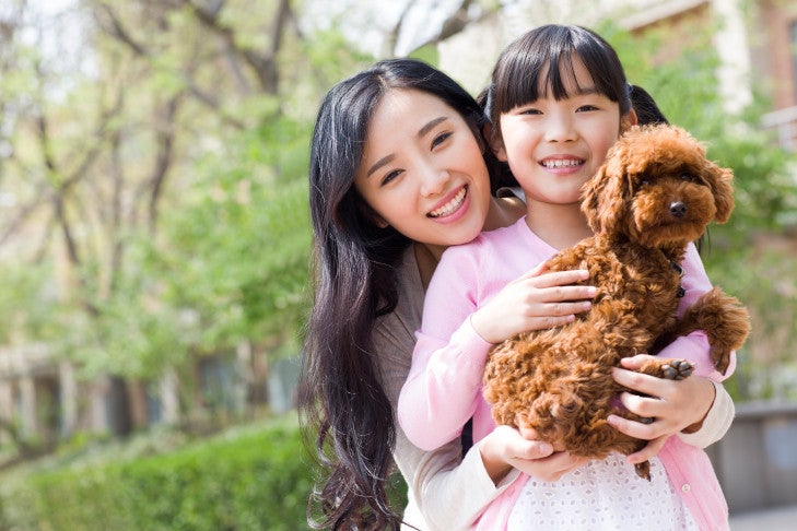 屋外で女の子と母親に抱かれるトイプードル。